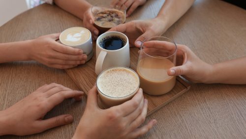 Friends drinking coffee at wooden table in cafe, closeup