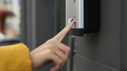 Voordeur-bel African-American woman ringing intercom with camera near building entrance, closeup